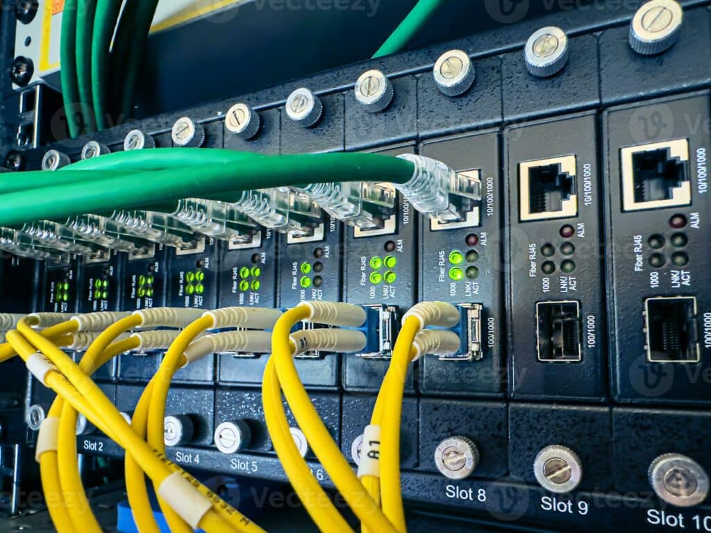 Network-Communication-Equipment-In-The-Datacenter-In-The-Server-Rack-With-Fiber-Optic-Hub-For-Digital-Communications-And-Internet-And-Cables-In-Big-Data-Center-Connecting-Lan-Cable-To-Mainframe-Photo Network Communication Equipment In The Datacenter In The Server Rack With Fiber Optic Hub For Digital Communications And Internet And Cables In Big Data Center Connecting Lan Cable To Mainframe Photo